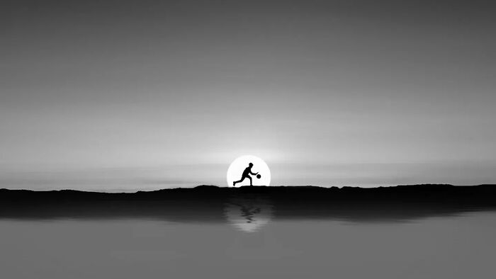 Silhouette of person playing basketball at sunset reflected on calm water, showcasing minimalism photography art style.
