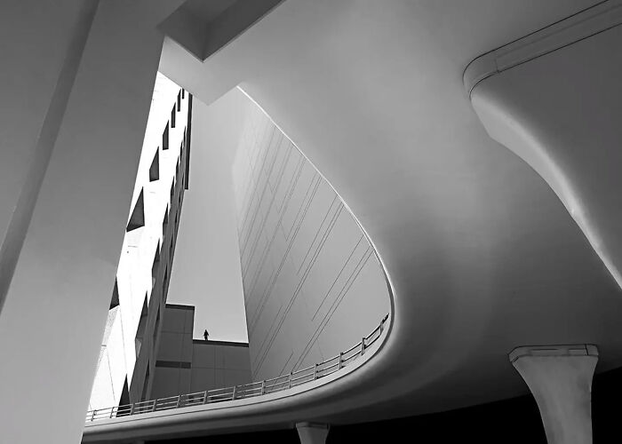 Black and white minimalist photograph of urban architecture featuring curved bridge and geometric building by photographer.