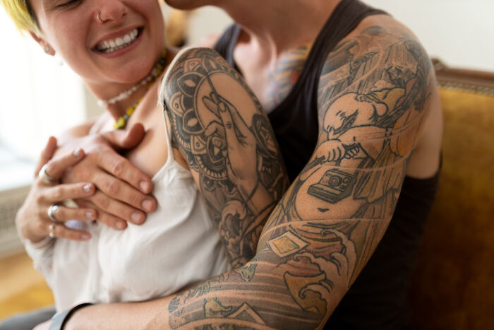 Close-up of a person with detailed tattoos on their arm embracing another, highlighting unique human body features.