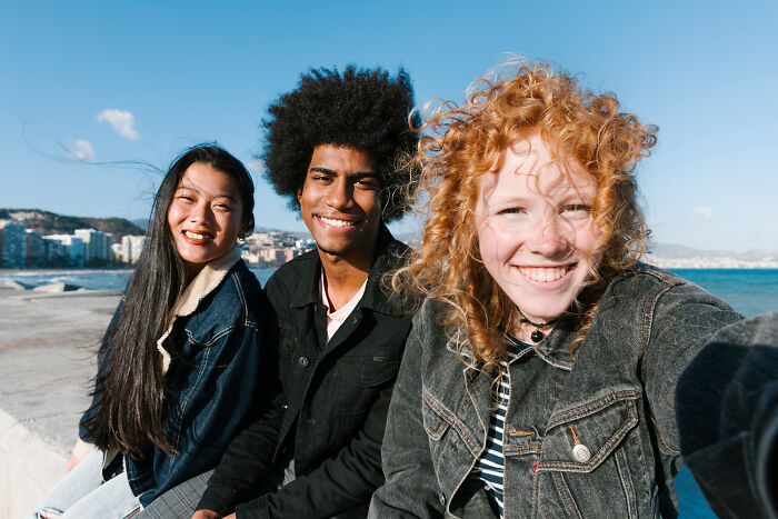 Three diverse friends smiling outdoors by the sea, highlighting fascinating human body features and facts.