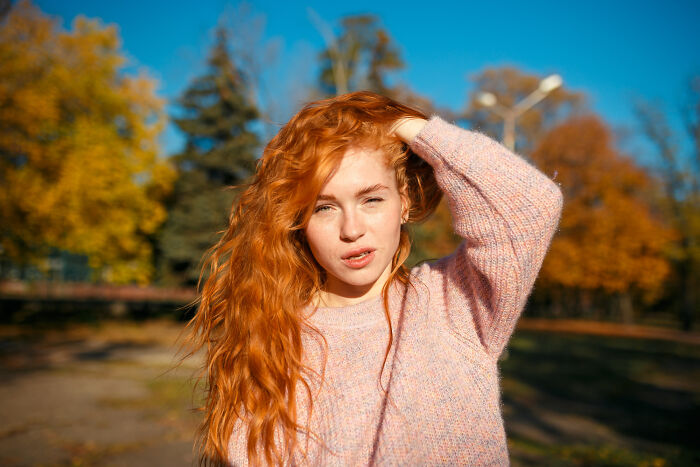 Young woman with red hair and fair skin in autumn park, highlighting fascinating human body features and unique traits.