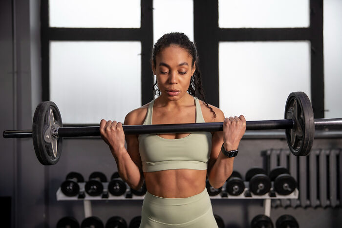 Woman in workout clothes lifting a barbell in a gym, demonstrating fascinating human body features and strength.
