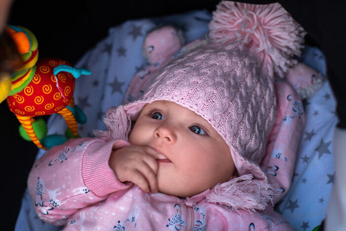 Baby wearing a pink knit hat and pajamas, showcasing fascinating human body features and developmental expressions.