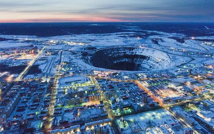 Night aerial view of a massive open-pit mine in a snowy landscape, showing a place that looks AI generated but is real.