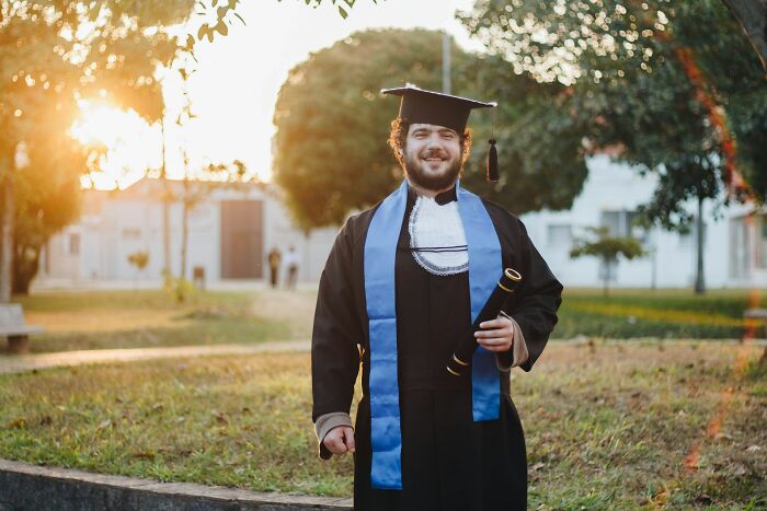 Graduate in cap and gown holding diploma outside at sunset, representing snobbish attitudes people shamed online.