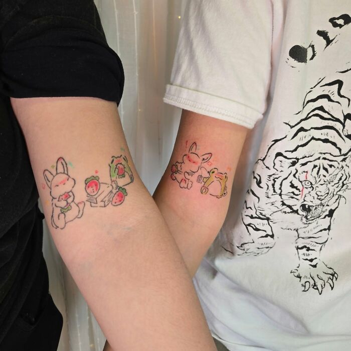 Matching wholesome tattoos of cute bunny and frog characters on inner forearms showing meaningful ink.
