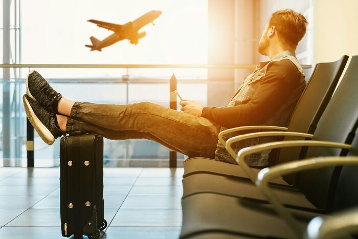 Man relaxing in airport lounge, watching plane take off, illustrating the digital nomad life and travel lifestyle.