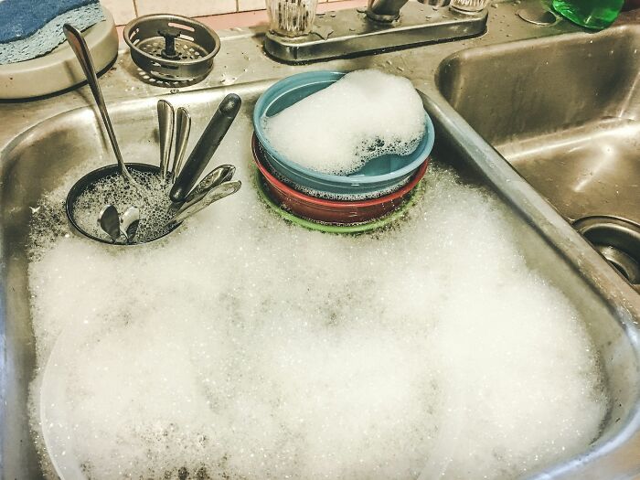 Soapy sink filled with dishes and utensils, showing an everyday thing people accidentally did wrong in cleaning.