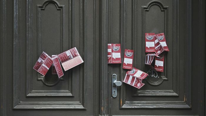 Several flyers cleverly placed on a dark wood door as a brilliantly sneaky act of revenge.