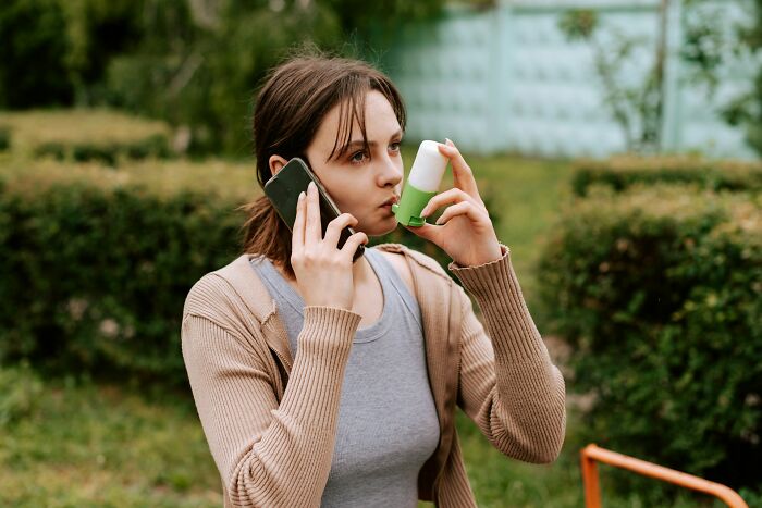 Woman using an inhaler and talking on the phone, illustrating ER staff challenges with difficult patients.