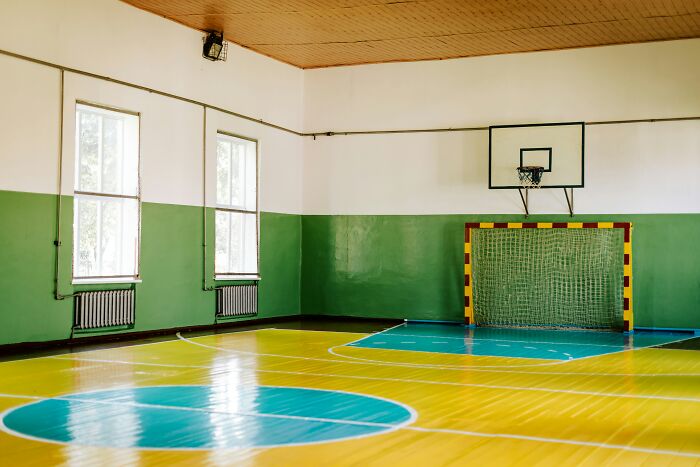 Empty indoor gym with basketball hoop and sports goal, illustrating signs someone is stuck in their high school era years later.