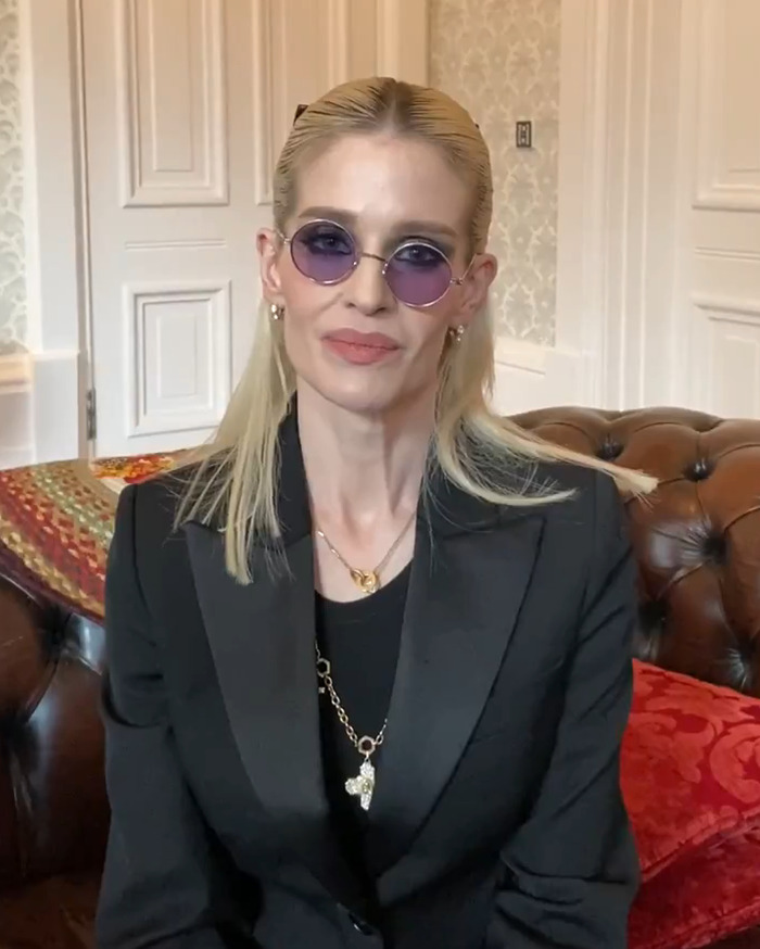 Kelly Osbourne wearing purple sunglasses and a black suit, speaking about her dad Ozzy on his 77th birthday indoors.