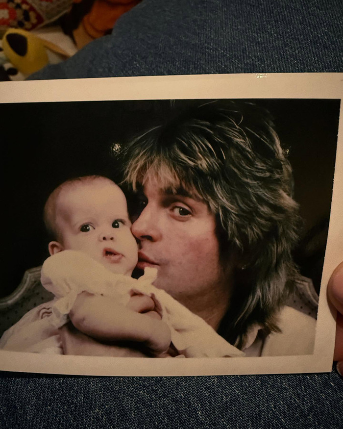 Vintage photo of Ozzy Osbourne holding a baby with fans commenting on Kelly Osbourne transformation and family talk.