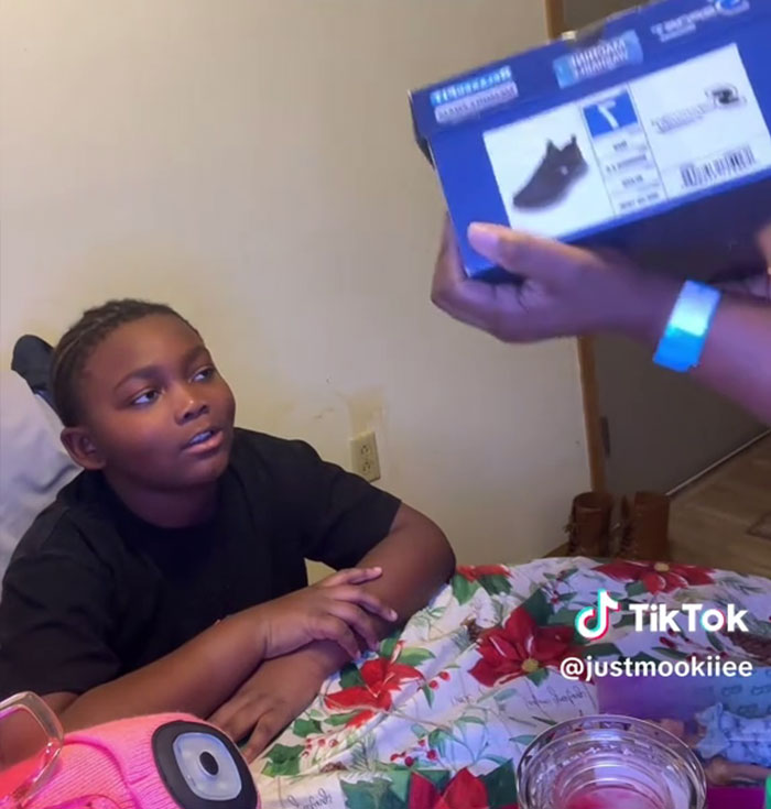 Boy sitting at a table with Christmas decorations, reacting to Angel Tree gifts being shown by an adult hand.