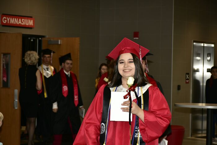 Young woman in red cap and gown holding a rose and diploma, symbolizing someone stuck in their high school era years later.