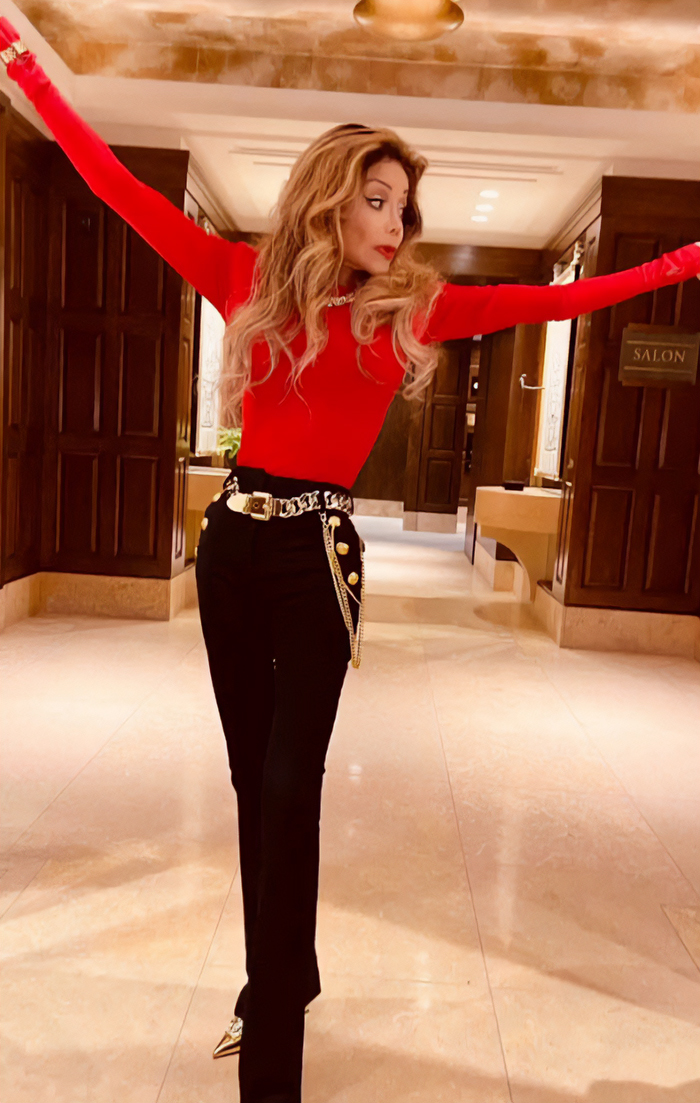 La Toya Jackson in red top and black pants, showing alarmingly slim appearance amid possible health issues indoors.