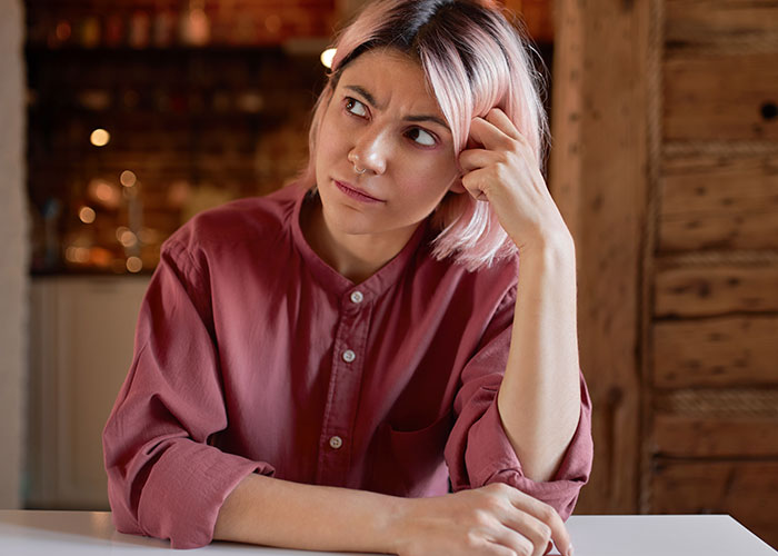 Young woman in pink shirt looking concerned while calling out sister-in-law for pretending to have a food allergy