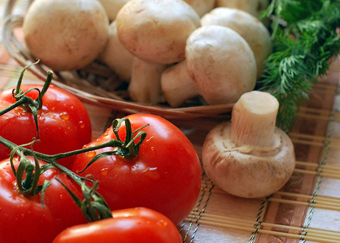 Fresh tomatoes and mushrooms on a table highlight common foods involved in food allergy discussions and concerns.