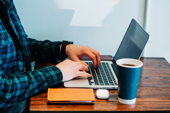 Person typing on laptop at wooden table with coffee cup and notebook, highlighting habits affecting mental and physical health long-term