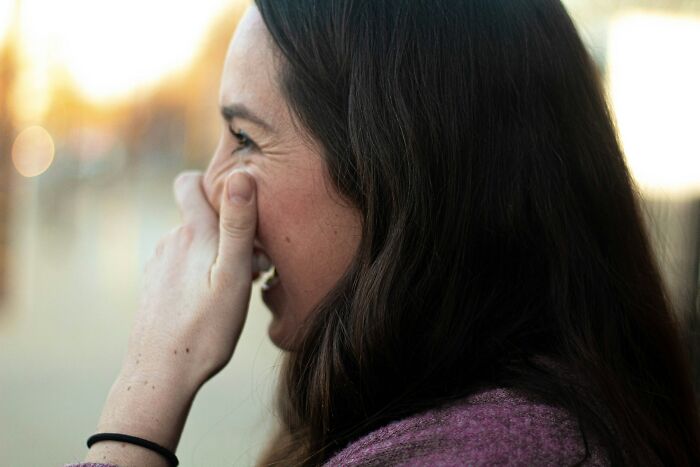 Woman with long hair in a purple sweater laughing and covering her mouth, capturing unexpected moments at funerals.