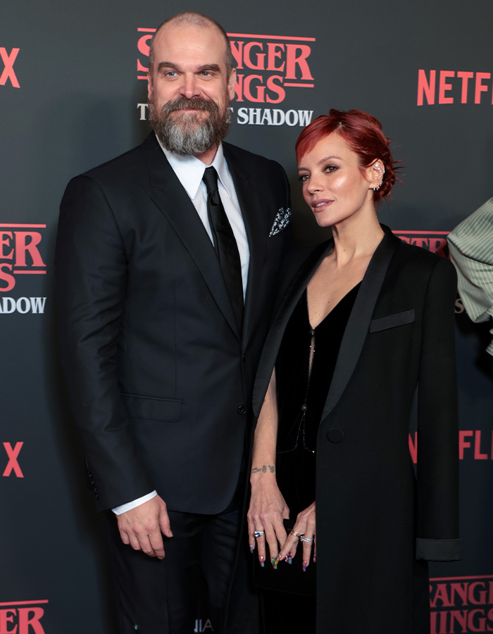 Lily Allen attending a red carpet event in a black coat and velvet dress, embracing a bearded man in a black suit.
