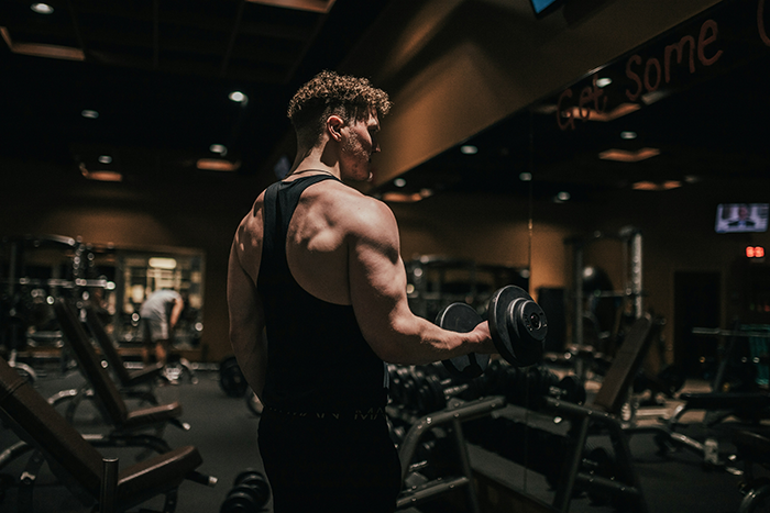 Muscular guy working out in a gym, showcasing strength and hunger for fitness in a dimly lit setting.