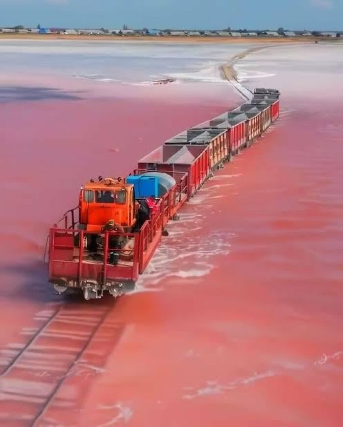 Train crossing vibrant pink salt flats, showcasing one of the remarkable places from around the world that look AI generated but are real.