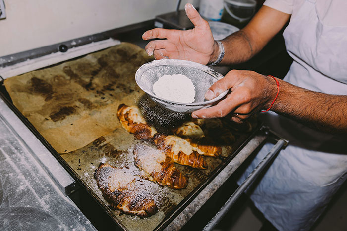 Pastry chef dusting pastries with powdered sugar, highlighting passion for pastries in baking process.