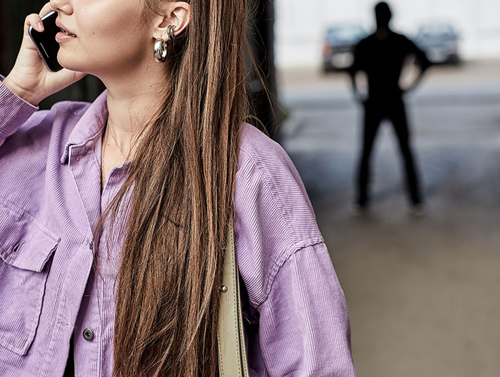 Woman making phone call in foreground with shadowy man in background symbolizing heroic Texas dad tracking phone.