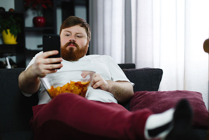 Man in casual clothes lounging with a bowl of chips, scrolling on his phone, representing guy vents online and girlfriend claps back.