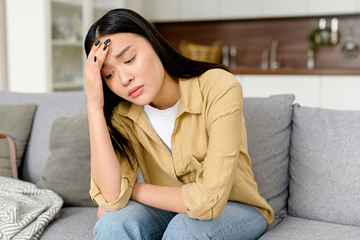 Young woman sitting on a couch looking worried and stressed, contemplating canceling wedding after family hires a PI
