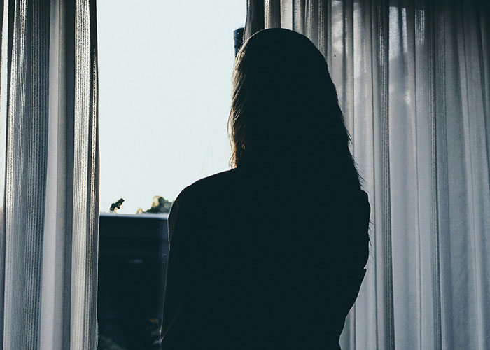 Silhouette of a woman standing by a window, symbolizing phone dependence affecting family relationships.