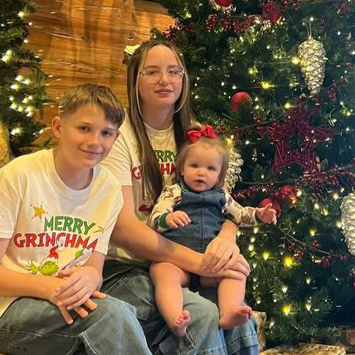 Three children sitting by a decorated Christmas tree during a family holiday gathering with a festive atmosphere.