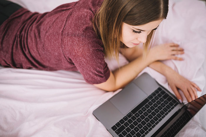 Woman lying on bed using laptop, representing moments of mansplained confidence with zero accuracy in online discussions.