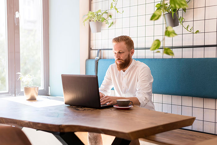 Man working confidently on laptop at wooden table in bright room, illustrating mansplained moments with peak confidence.
