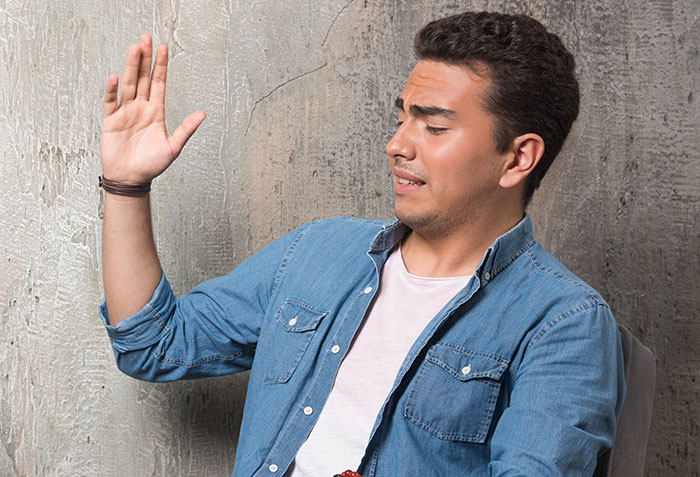Man in denim shirt raising hand defensively, illustrating mansplained confidence with zero accuracy concept.