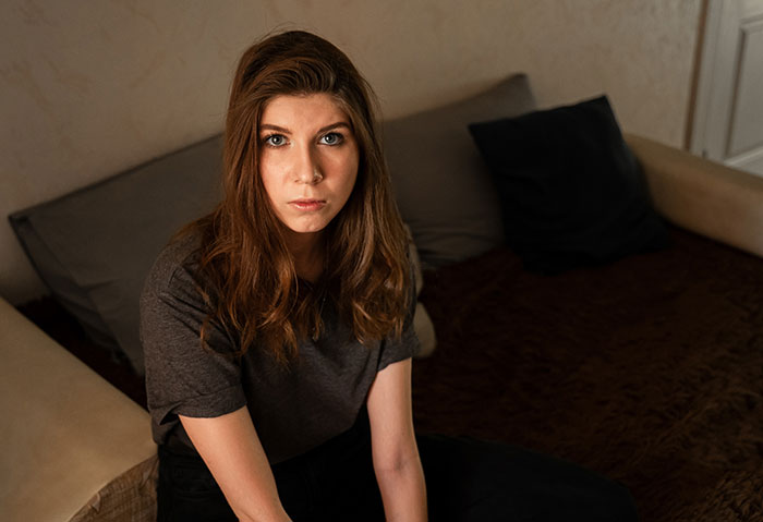 Young woman sitting on a couch with a serious expression, illustrating mansplained moments with peak confidence and zero accuracy.