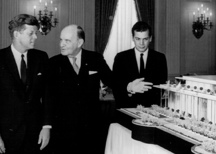 Black and white photo showing three men in suits examining a detailed architectural model of the Kennedy Center. Black and white photo showing three men in suits examining a detailed architectural model of the Kennedy Center.