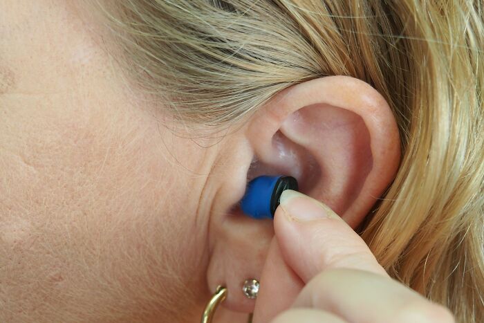 Person inserting a blue earplug indicating habits that might affect mental and physical health long-term.