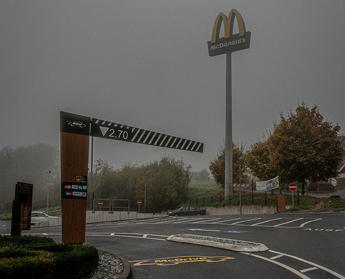 McDonald&rsquo;s drive-thru entrance with height barrier and logo on a foggy day at an empty parking lot.
