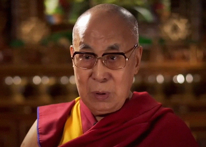 Elderly man wearing glasses and traditional robes speaking in an interview about famous people they have met.