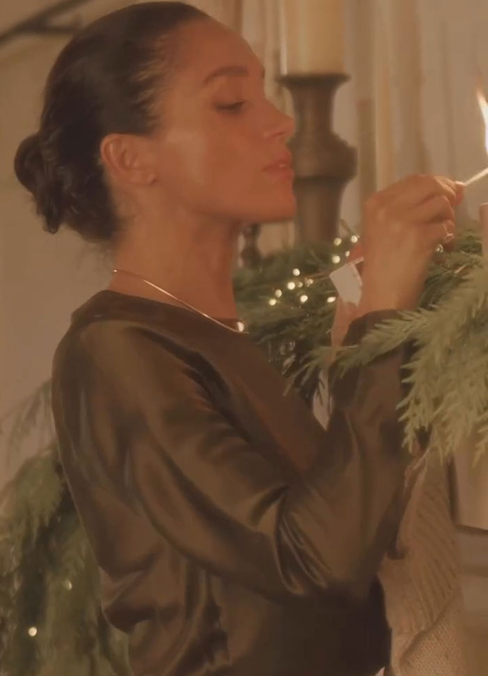 Meghan Markle lighting a candle by Christmas decorations, linked to Prince Harry split rumors during holiday season.