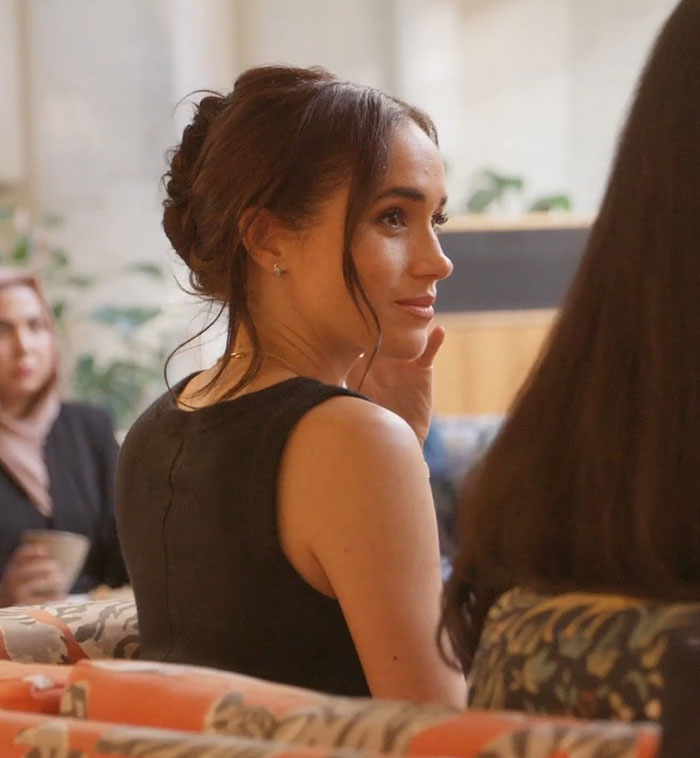 Meghan Markle in a black dress sitting indoors with an attentive expression, related to Prince Harry holiday snap manipulation.