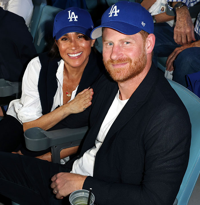 Prince Harry and Meghan Markle wearing matching LA caps, smiling together at an event amid holiday snap manipulation claims.