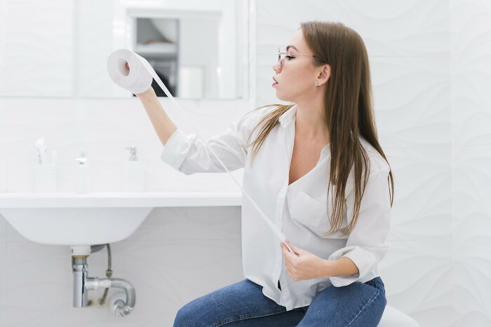 Woman sitting in a bathroom holding and examining a roll of toilet paper, illustrating insights about women from relationships.