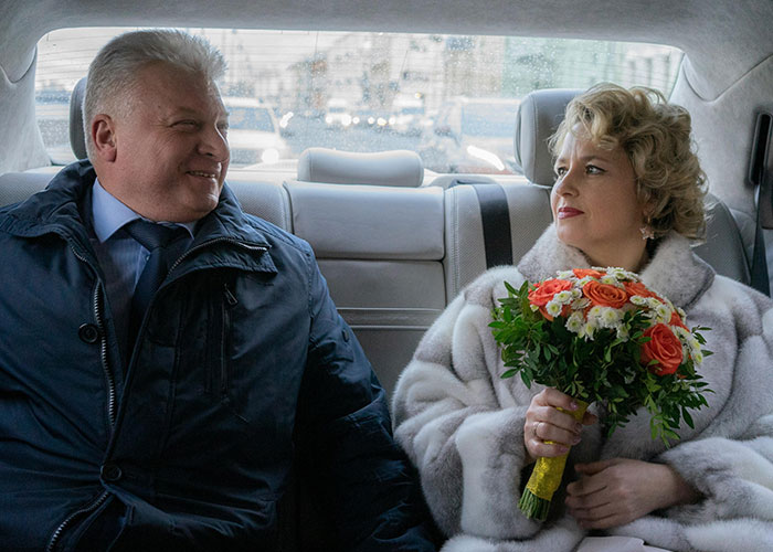 Couple sitting in a car during a wedding, bride holding bouquet, reflecting mil demands and wedding venue changes stuck in storm.