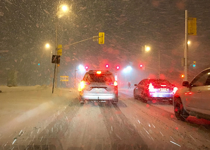 Cars stuck in snowy storm while military demands wedding venue changes cause delays on road at night.