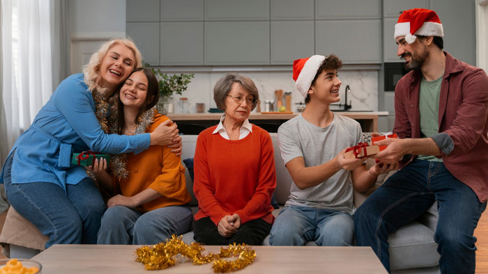 Family celebrating Christmas with grandma in a festive living room, showing playful gift exchange and holiday competition.