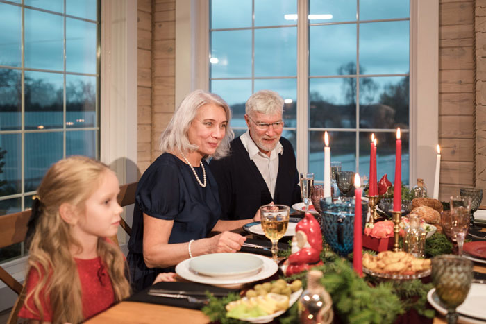 Family gathered around a mil house Christmas dinner table with festive decorations and a dog nearby.