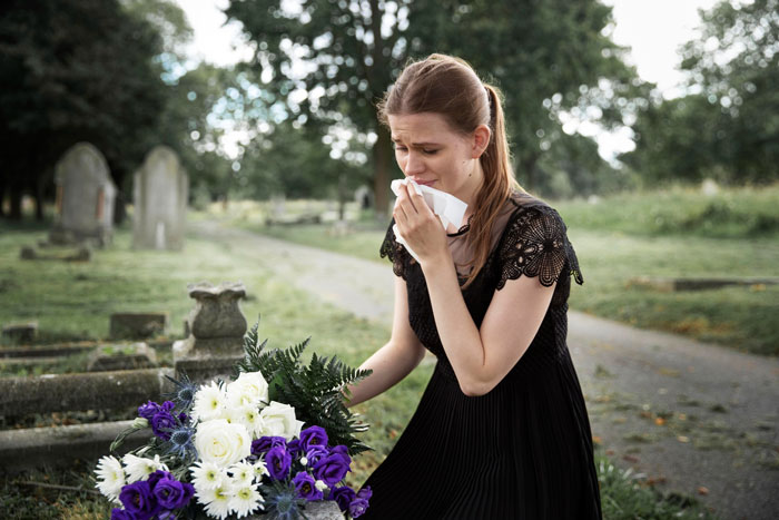 Woman in black mourning at a grave with flowers in a peaceful cemetery setting, reflecting mil house Christmas dog theme.